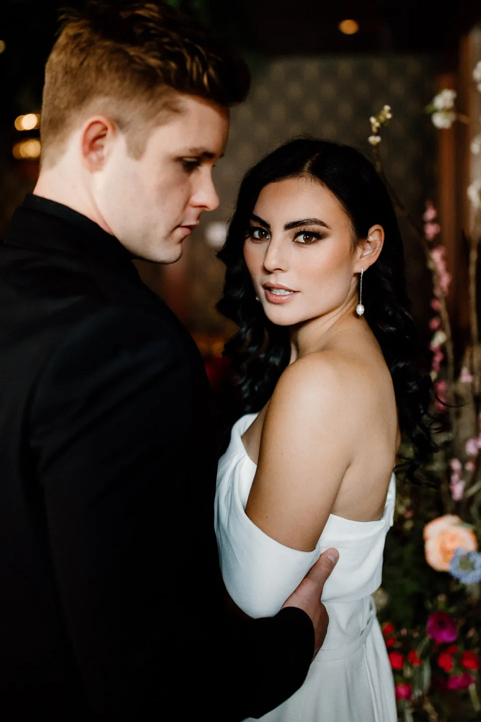 Bride with polished dark waves and luminous makeup beside her partner