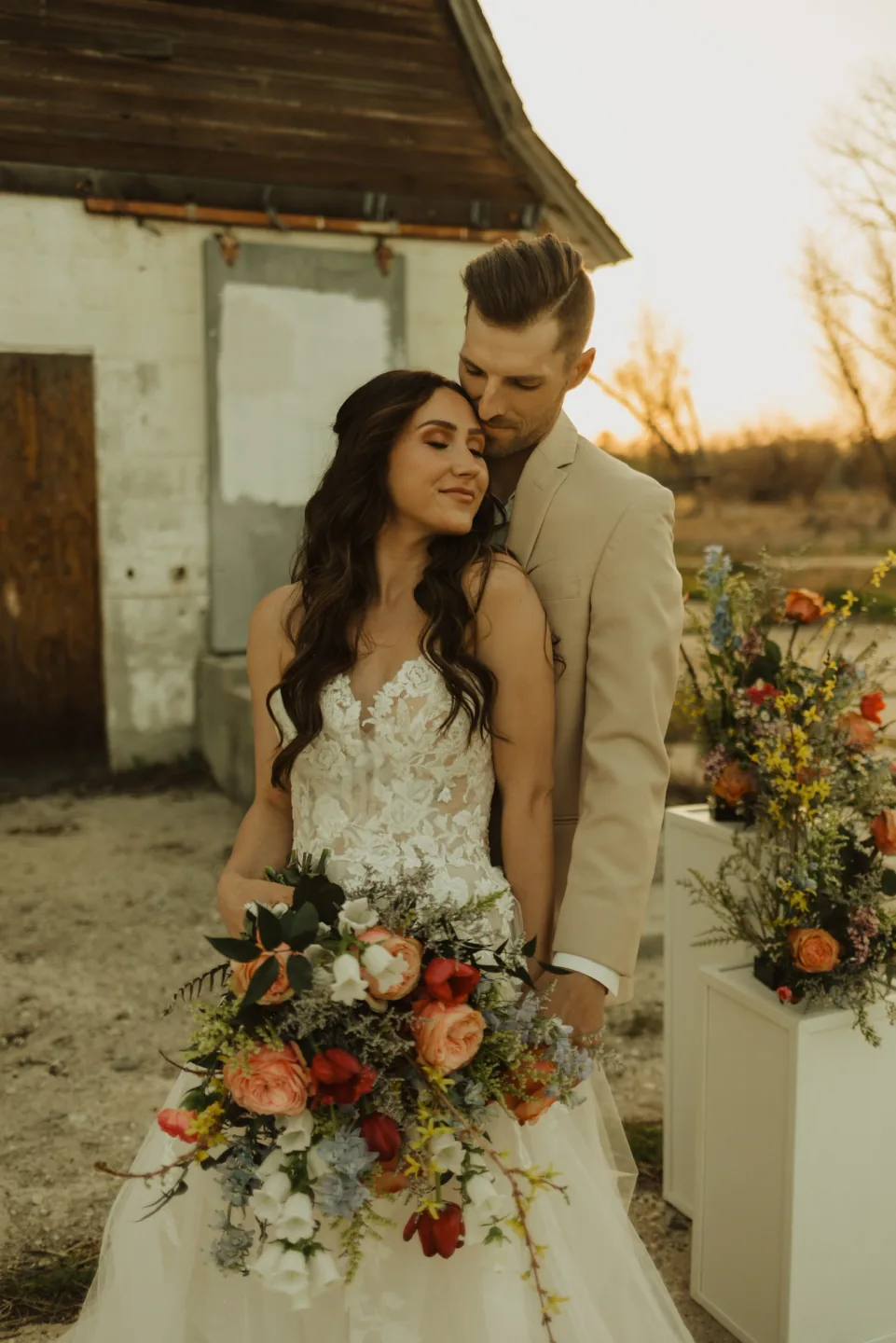 Bride with long dark waves and soft makeup standing with her partner outdoors