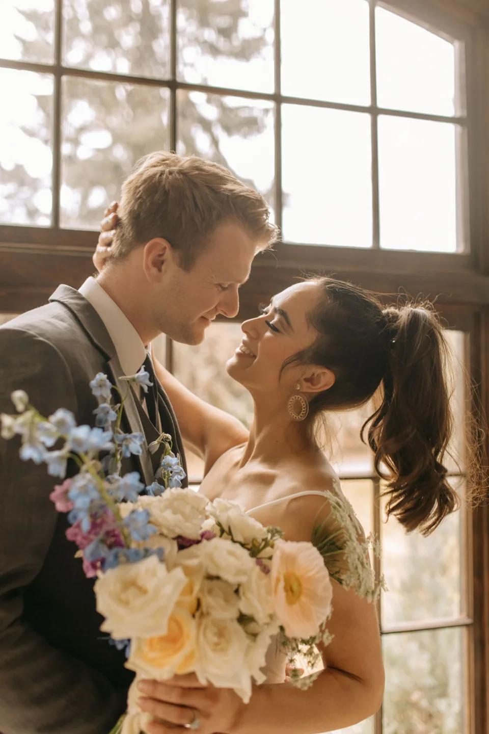 Bride with a high ponytail smiling at her partner by a window