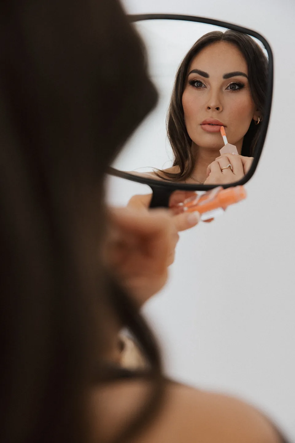 Woman applying lip color while looking into a hand mirror